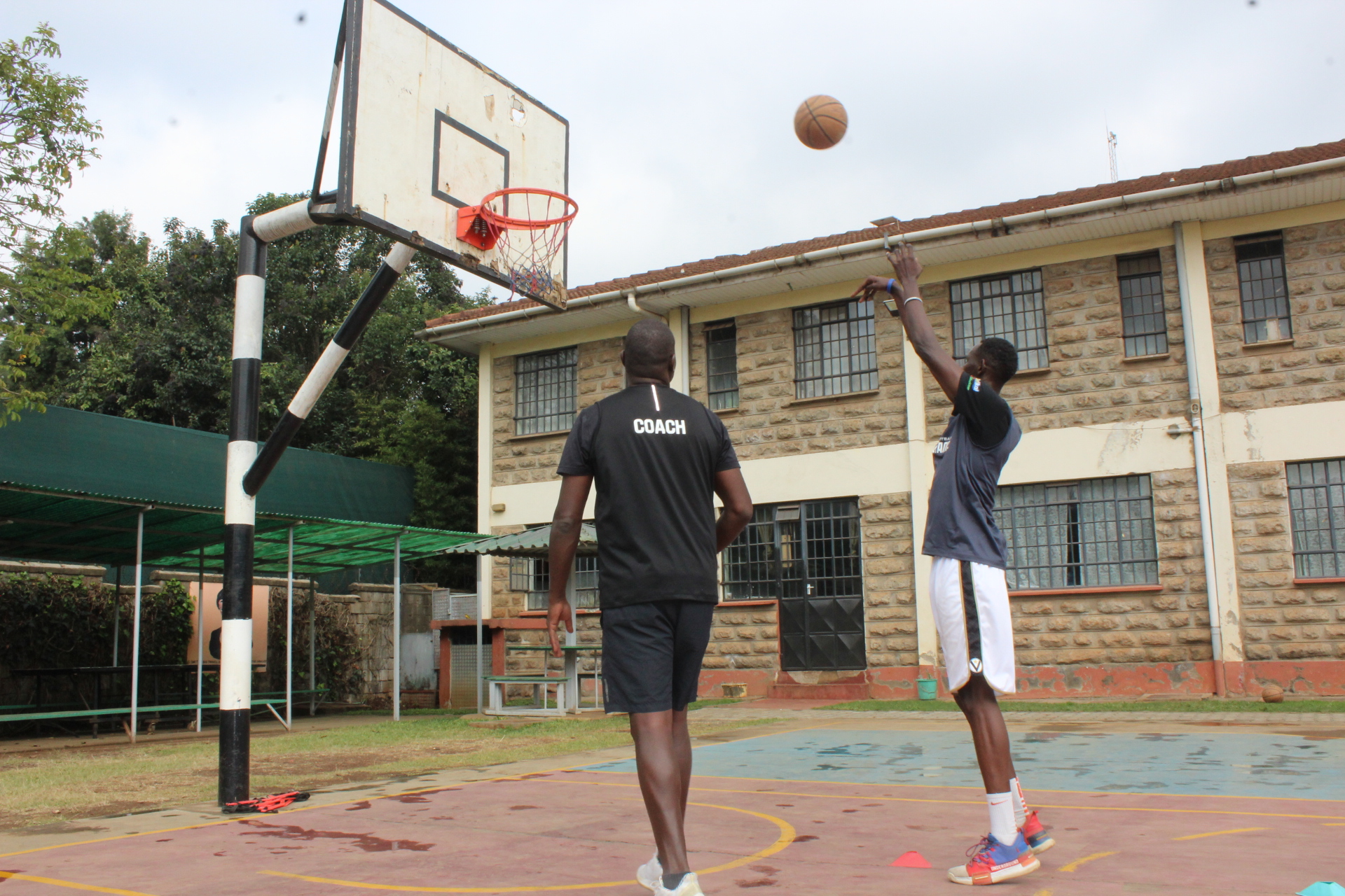 A basketball player shoots as a coach watches from the court